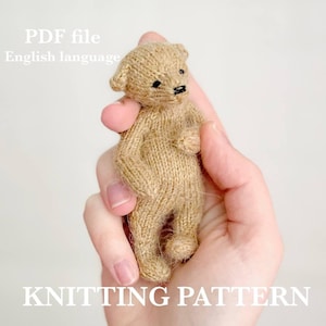 Puede incluir: Un pequeño oso de peluche tejido, en tonos beige y marrón, se sostiene en una mano. El oso tiene pequeños ojos negros y una nariz negra. La imagen incluye el texto "PDF file English language" y "KNITTING PATTERN".