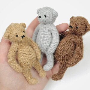 Peut inclure: Trois petits ours en peluche tricot&eacute;s, de couleur beige, grise et marron, sont tenus dans une main. Chaque ours a de petits yeux noirs et un nez cousu. Les ours sont doux et c&acirc;lins, parfaits pour une collection de jouets.