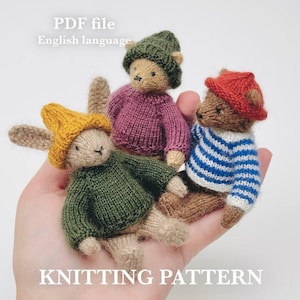 Könnte beinhalten: Drei kleine, handgestrickte Tierfiguren: ein Hase und zwei Bären. Der Hase trägt einen gelben Hut und einen grünen Pullover. Ein Bär trägt einen roten Hut und einen blau-weiß gestreiften Pullover. Der andere Bär trägt einen grünen Hut und einen lila Pullover. Text: PDF file, English language, KNITTING PATTERN.