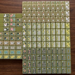 Peut inclure: Une collection de tuiles de mah-jong vert olive dispos&eacute;es en grille. Les tuiles pr&eacute;sentent divers motifs grav&eacute;s, notamment des caract&egrave;res chinois, des tiges de bambou, des motifs circulaires, des motifs floraux et du texte directionnel.