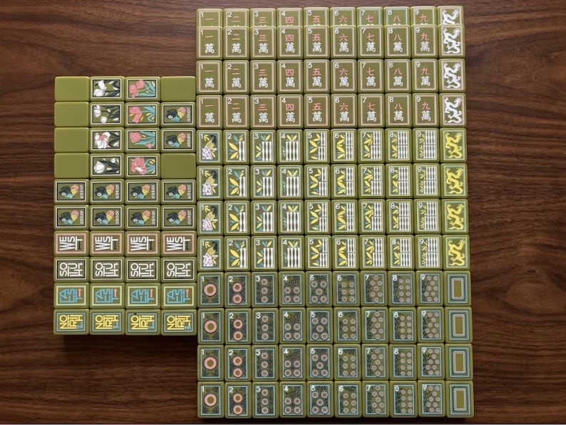 Peut inclure: Une collection de tuiles de mah-jong vert olive dispos&eacute;es en grille. Les tuiles pr&eacute;sentent divers motifs grav&eacute;s, notamment des caract&egrave;res chinois, des tiges de bambou, des motifs circulaires, des motifs floraux et du texte directionnel.