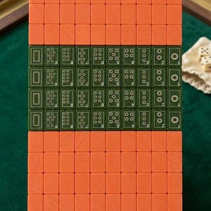 Peut inclure: Un ensemble de tuiles de mah-jong rectangulaires dispos&eacute;es en grille. Les tuiles pr&eacute;sentent un design bicolore avec des dos orange unis et des faces vert fonc&eacute;. Les tuiles vertes affichent des points num&eacute;riques, des motifs floraux et du texte.