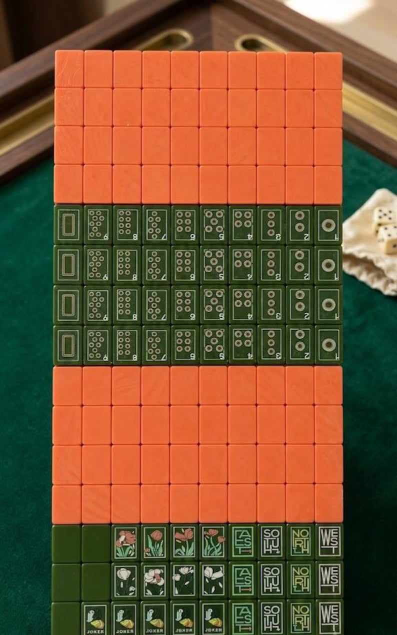 Peut inclure: Un ensemble de tuiles de mah-jong rectangulaires dispos&eacute;es en grille. Les tuiles pr&eacute;sentent un design bicolore avec des dos orange unis et des faces vert fonc&eacute;. Les tuiles vertes affichent des points num&eacute;riques, des motifs floraux et du texte.