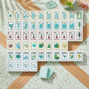 May include: A set of white Mahjong tiles arranged in rows, featuring blue and green illustrations of marine life, plants, and numbered characters. The bottom row displays the letters N, E, W, S in blue, with two additional blank tiles placed below.