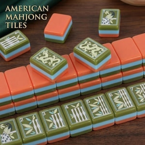 Peut inclure: Un ensemble de tuiles de Mahjong am&eacute;ricain pr&eacute;sentant un design tricolore avec des couches orange, bleu clair et vert olive. Les tuiles affichent diverses illustrations grav&eacute;es, notamment des dragons, des tiges de bambou et des oiseaux.