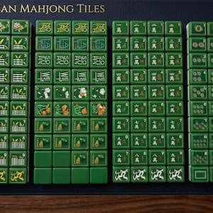 Peut inclure: Un ensemble de tuiles de Mahjong am&eacute;ricain vertes dispos&eacute;es en quatre colonnes sur une surface bleu fonc&eacute;. Les tuiles pr&eacute;sentent diverses illustrations dont du bambou, des fleurs, des dragons et du texte comme Joker, North, South, East et West.