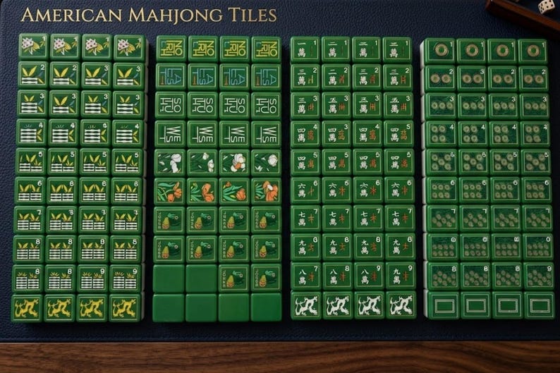 Peut inclure: Un ensemble de tuiles de Mahjong am&eacute;ricain vertes dispos&eacute;es en quatre colonnes sur une surface bleu fonc&eacute;. Les tuiles pr&eacute;sentent diverses illustrations dont du bambou, des fleurs, des dragons et du texte comme Joker, North, South, East et West.