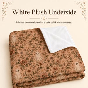 May include: A folded blanket featuring a tan background with a repeating pattern of small ghosts, flowers, and stars. The text White Plush Underside and Printed on one side with a soft solid white reverse is visible above the blanket.