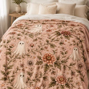 May include: A soft plush blanket in a dusty pink hue featuring a repeating pattern of white ghosts, large blooming flowers, and small stars. The design includes intricate green foliage and stems connecting the floral and ghost motifs throughout.