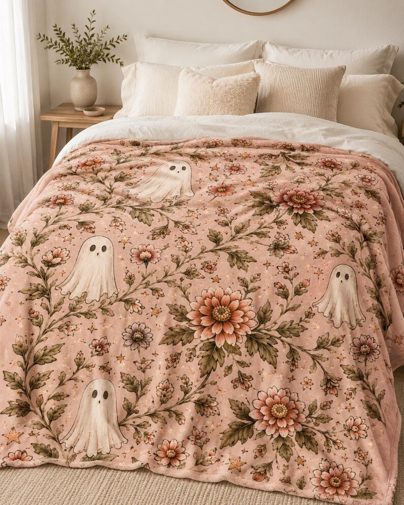 May include: A soft plush blanket in a dusty pink hue featuring a repeating pattern of white ghosts, large blooming flowers, and small stars. The design includes intricate green foliage and stems connecting the floral and ghost motifs throughout.