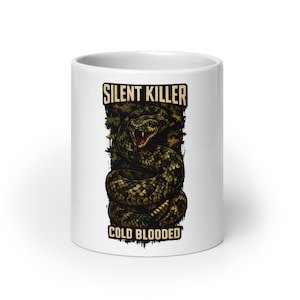 May include: A white ceramic mug featuring a graphic illustration of a coiled snake with its mouth open, displaying fangs. The text SILENT KILLER is printed in a distressed font above the snake, and COLD BLOODED is printed below in the same style.