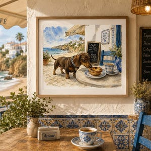 Puede incluir: Una impresión en acuarela enmarcada representa un perro salchicha en una mesa de café, oliendo un pastel. La escena incluye una vista costera, un letrero de café y un menú de pizarra. Una taza de café está sobre la mesa, y el café está decorado con azulejos azules y blancos.