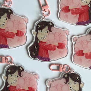 Peut inclure: Porte-clés en acrylique représentant une jeune fille de dessin animé étreignant un cochon rose. La fille a de longs cheveux bruns avec des étoiles, portant une chemise rouge et une jupe violette. Chaque porte-clés a un fermoir rose.