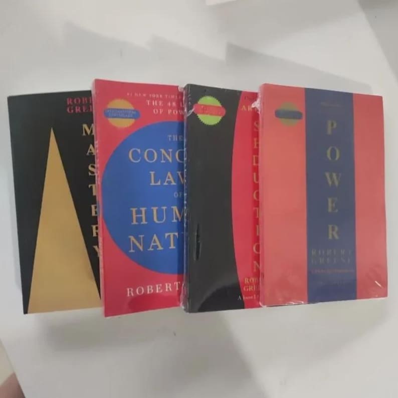 May include: Four hardcover books by Robert Greene are displayed. The book covers are in various colors, including black, red, and blue. Titles include "Mastery", "The 48 Laws of Power", "The Concise Laws of Human Nature", and "Seduction".