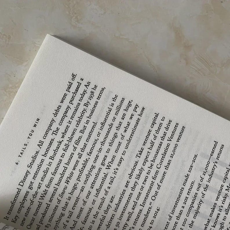 May include: Open book page with printed text. The text includes the title "6. TAILS. YOU WIN" and paragraphs discussing business and investment strategies. The page is white with black text.