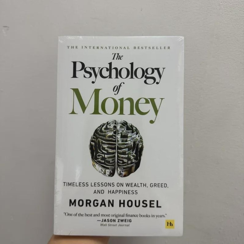 May include: A paperback book titled "The Psychology of Money" with a white cover. The title is in large green letters, with a brain graphic. The author's name is Morgan Housel. The book is described as containing timeless lessons on wealth, greed, and happiness.