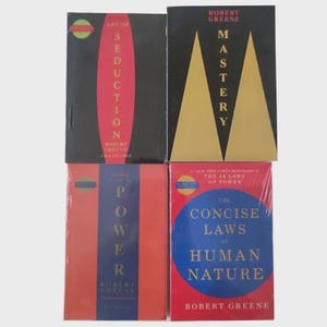 May include: Four hardcover books by Robert Greene are displayed. The books have titles such as "Art of Seduction", "Mastery", "Power", and "The Concise Laws of Human Nature". The covers are black, red, and blue with white and gold lettering.