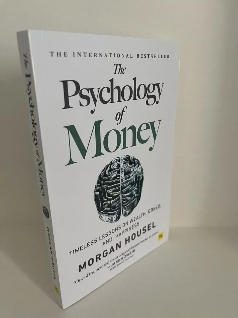 May include: A hardcover book titled "The Psychology of Money" with a white cover. The title is in large black letters with the word "Money" in green. The book features a brain graphic and author's name.