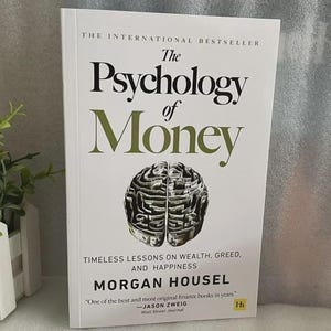 May include: A hardcover book titled "The Psychology of Money" with a white cover and green text. The cover features a brain-shaped illustration and the author's name, Morgan Housel. The book is described as a bestseller with lessons on wealth, greed, and happiness.