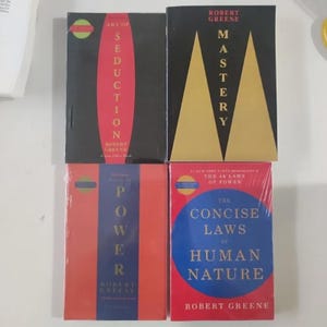 May include: Four hardcover books by Robert Greene are displayed. The books have various color schemes, including black, red, and blue. Titles include "Art of Seduction," "Mastery," "Power," and "The Concise Laws of Human Nature."