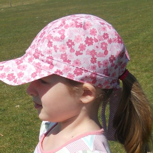 May include: A pink and white floral baseball cap with a ponytail holder attached to the back. The cap has a white brim and a pink crown with a floral pattern.