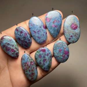 Può includere: Otto pietre preziose cabochon lucidate numerate da uno a otto, caratterizzate da una matrice screziata blu e verde con vivaci inclusioni rosa magenta. Ogni pietra ha una superficie liscia e arrotondata, con forme ovali o a goccia.