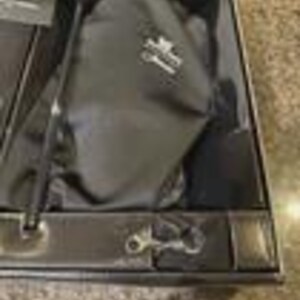 Pu&ograve; includere: Una scatola nera contenente una custodia in tessuto nero con un logo bianco e una sottile penna stilo nera. La scatola presenta uno scomparto interno sagomato progettato per tenere gli oggetti in posizione, con una piccola clip metallica in basso.