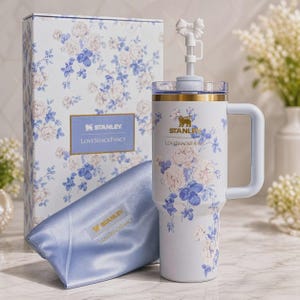Puede incluir: Un vaso Stanley LoveShackFancy azul claro con estampado floral, borde dorado, asa y un adorno de lazo blanco en la pajita. Incluye una caja floral a juego y una bolsa de sat&eacute;n azul claro con el logotipo de Stanley LoveShackFancy.