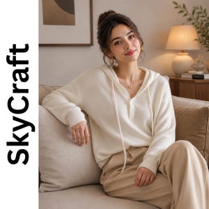 May include: A cream-colored long-sleeve waffle knit hoodie featuring a henley-style button placket at the neckline and matching drawstring cords. The garment is paired with beige trousers. The text SkyCraft is visible on the left side of the image.