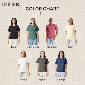 Op de afbeelding: Een kleurenkaart voor Comfort Colors T-shirts, met zeven verschillende kleuren: zwart, lichtgroen, karmozijnrood, ivoor, wit, peper en middernacht. Elke kleur wordt getoond op een persoon die het T-shirt draagt.