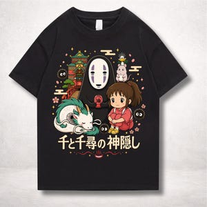 Op de afbeelding: Zwart t-shirt met een kleurrijke afbeelding uit de animatiefilm Spirited Away. Het ontwerp bevat personages als No-Face, Chihiro en Haku de draak, met Japanse tekst eronder. Een levendige en gedetailleerde illustratie.