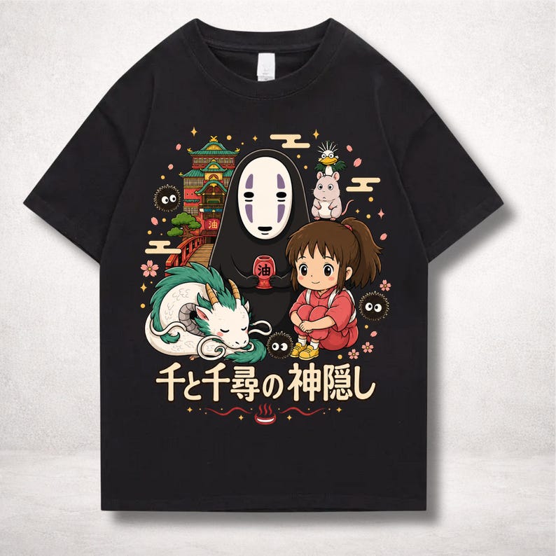Op de afbeelding: Zwart t-shirt met een kleurrijke afbeelding uit de animatiefilm Spirited Away. Het ontwerp bevat personages als No-Face, Chihiro en Haku de draak, met Japanse tekst eronder. Een levendige en gedetailleerde illustratie.
