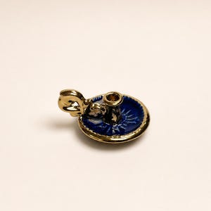 Pode incluir: Um pequeno castiçal de cerâmica com uma base circular azul-profundo de acabamento brilhante e uma borda dourada. A peça inclui um encaixe cilíndrico central para vela e uma alça decorativa em tom dourado com formato de alça estilizada.
