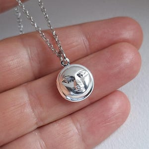 Può includere: Una collana d'argento con un ciondolo rotondo che presenta un viso in rilievo. Il ciondolo ha un diametro di circa 2,5 cm.