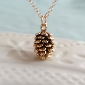 May include: A gold necklace featuring a detailed pine cone pendant. The pendant is crafted from metal and has a realistic design.