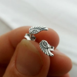 May include: A pair of silver earrings with a wing design and a small clear stone in the center of each wing.