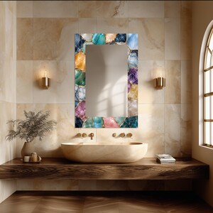 May include: A rectangular wall mirror featuring a decorative frame composed of multicolored, polished agate-style stone slices in shades of blue, purple, pink, gold, and white, with thin gold-toned metallic accents between each stone segment.
