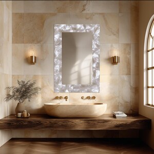 May include: A rectangular wall mirror featuring a wide, textured frame with a shimmering, pearlescent white finish. The mirror is mounted above a smooth, oval-shaped beige stone vessel sink resting on a dark wooden floating vanity shelf.