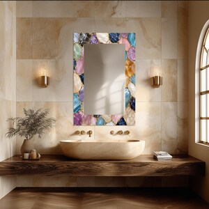 May include: A rectangular wall mirror featuring a decorative frame composed of multicolored, polished stone-like segments in shades of blue, purple, pink, white, and amber, arranged in a mosaic pattern with gold-toned grout lines between each piece.