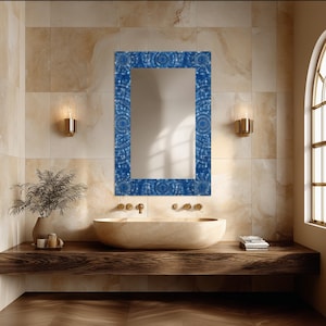 May include: A rectangular wall mirror featuring a decorative frame with a deep blue mosaic pattern composed of small, circular, and square tiles. The mirror is mounted vertically, reflecting the surrounding space with a clear, reflective glass surface.