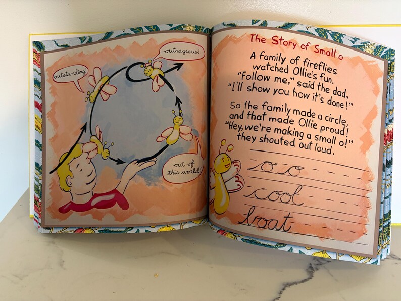 May include: An open children's book with two pages showing illustrations of yellow fireflies and a person. The left page shows fireflies flying in a circle with speech bubbles saying outstanding, outrageous, and out of this world. The right page has the text The Story of Small o and practice lines for cursive writing.