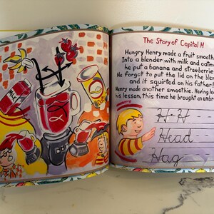 May include: An open children's book page featuring a colorful illustration of a blender, fruit, and milk, alongside the text The Story of Capital H. The right page shows a boy and cursive writing practice lines with the words H, Head, and Hag.