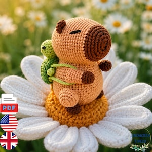 May include: A crochet capybara toy with light brown yarn, dark brown snout and feet, and closed eyes. A small green crochet turtle is attached to its back. The capybara sits on a large white crochet daisy flower with a yellow centre.