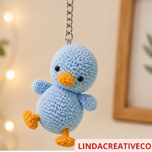 May include: A crocheted blue duck keyring with orange beak and feet, and black eyes. The duck is suspended from a silver chain. The text "LINDA CREATIVE CO" is at the bottom of the image.