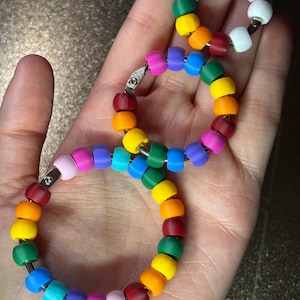 May include: Three circular metal rings of varying sizes, each threaded with a sequence of matte-finish plastic beads in a vibrant rainbow spectrum including red, orange, yellow, green, blue, purple, pink, and white, arranged in a repeating pattern.