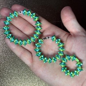 May include: Three circular metal rings of varying sizes, each featuring a series of translucent, spiky, lime green and teal beads strung along the circumference. The beads have a faceted, star-like shape and are arranged in a repeating colour pattern.