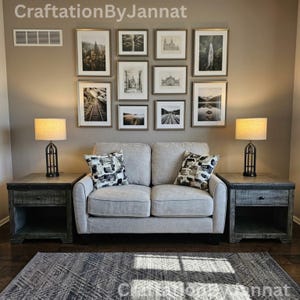 May include: A light gray loveseat with two patterned throw pillows, flanked by two dark wood end tables with lamps. Above the loveseat, a gallery wall features nine framed prints in various sizes, including landscapes and architectural sketches.