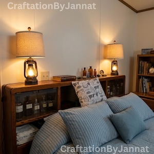 May include: A wooden headboard with integrated shelving and glass-front cabinets, topped with two rustic lantern-style lamps featuring beige fabric shades. The shelves hold glass bottles and a book, while the bed is dressed in blue striped bedding.