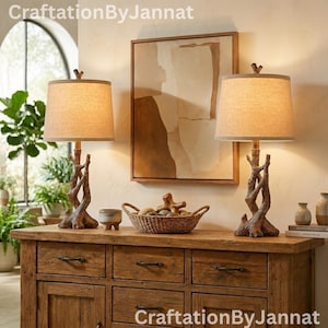 May include: Two decorative table lamps with a rustic, natural wood branch design. Each lamp has a beige fabric shade and sits on a wooden dresser. A woven basket and artwork are also on the dresser. The text "CraftationByJannat" is visible.