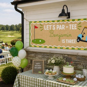 May include: A golf-themed birthday party scene. A banner reads "Let's Par-Tee Benjamin is Three!" with a golf cart illustration. A table is set with a cake, cupcakes, and golf ball decorations. Green and white balloons add to the festive atmosphere.